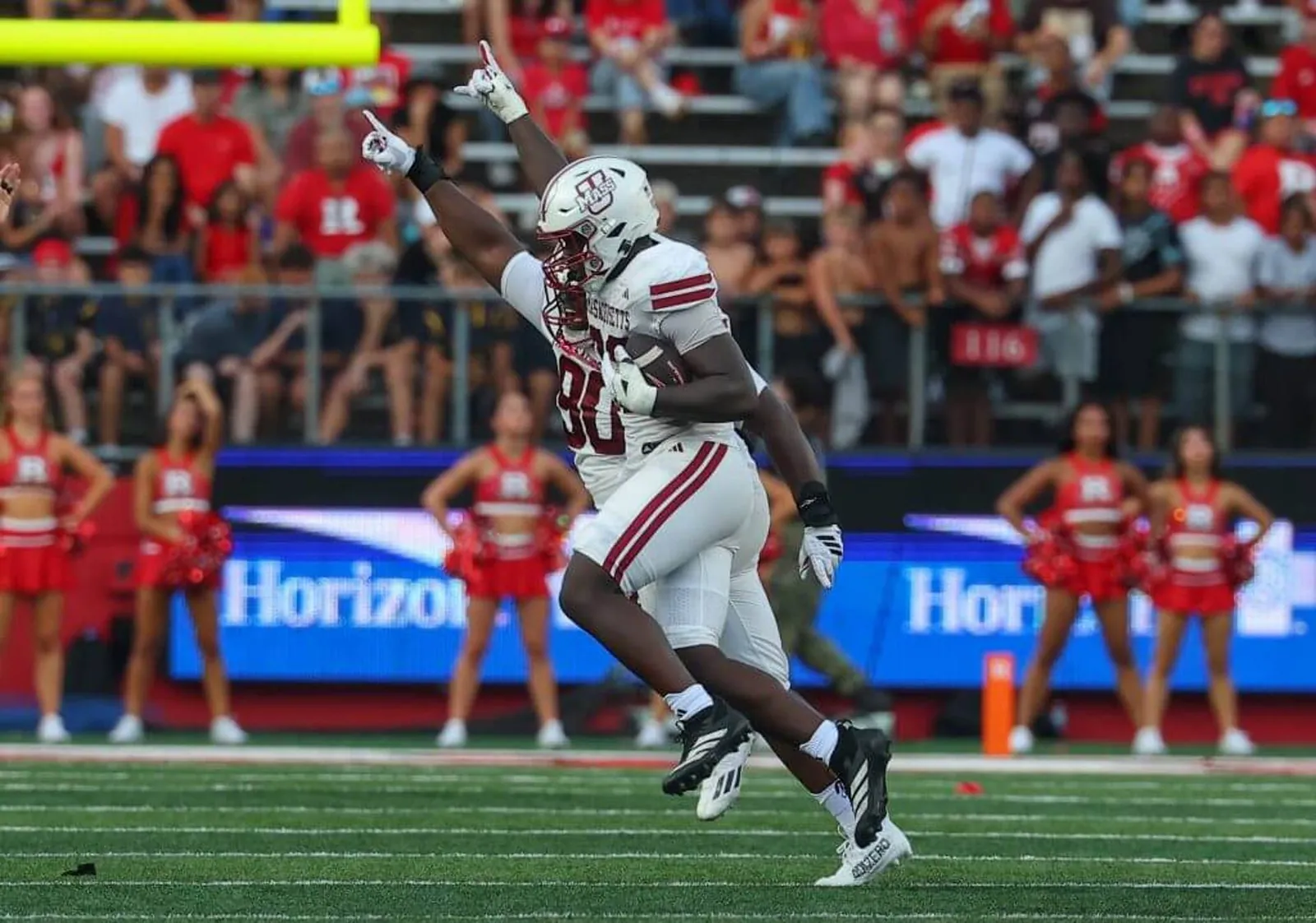 UMass' Romando Johnson points his right index finger to the sky while cradling a football in his left arm during a game against Rutgers.